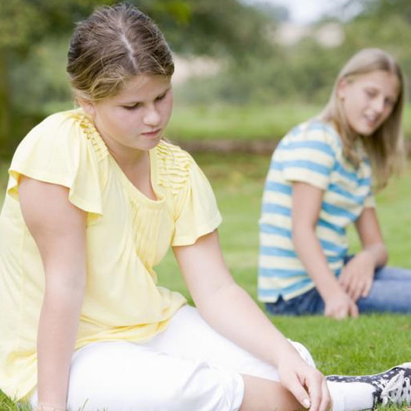 Girl looking down as a girl in background sneers at her.