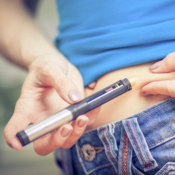 Woman holding an insulin pen against her stomach.