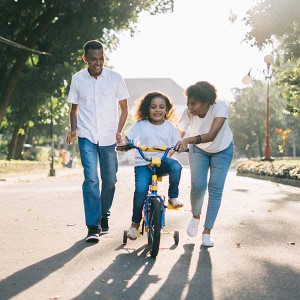 Parents walking with daughter on training bike.