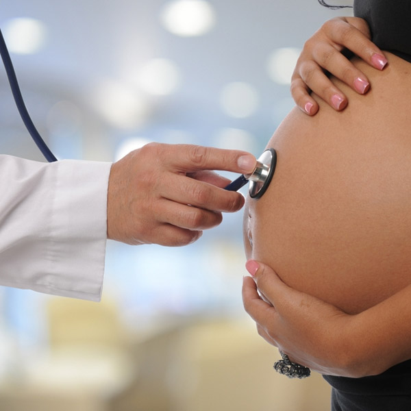 Doctor holding a stethoscope against a pregnant stomach.